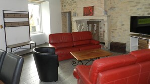 A living room with a red sofa, a wooden coffee table, and a television. - Charming Countryside Farmhouse with Garden, Terrace & Spacious Rooms (Avessé)