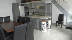 A modern kitchen with a central island, built-in appliances, and a dining area with a wooden table and chairs. - Charming Countryside Farmhouse with Garden, Terrace & Spacious Rooms (Avessé)