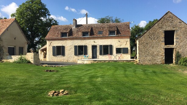 A two-story stone house with a sloped roof, a small front porch with outdoor seating, and a well-maintained lawn. - Charming Countryside Farmhouse with Garden, Terrace & Spacious Rooms (Avessé)