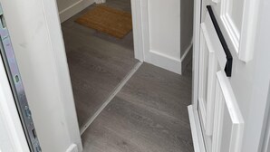 A hallway with a white door, a brown doormat, and a red electrical outlet on the wall.