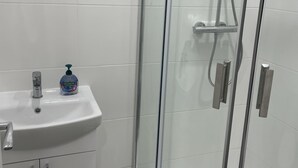 A bathroom with a glass-enclosed shower, a sink with a soap dispenser, and a cabinet.