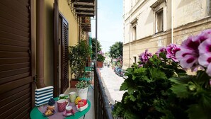 A narrow balcony with a table set for breakfast, potted plants, and a view of a street with parked cars and buildings. - Cassari Cottage (Palermo)