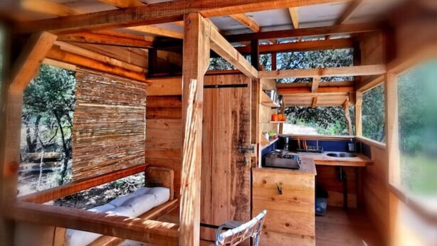 Une cabane en bois rustique, dotée d’un aménagement simple, comprenant un coin salon et une petite kitchenette.