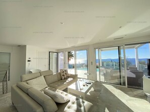 A modern living room with a sofa, a coffee table, and a view of a pool and mountains. - Modern villa with pool and air conditioning (Cavalaire-sur-Mer)