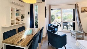 A dining area with a wooden table and blue chairs, a hanging light fixture, and a view through a glass door to an outdoor patio. - Ground Floor Apartment, 3 Rooms, 2 Terraces, 100m from Beach, A/C, Parking, WiFi Optional (Lumio)