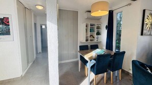 A dining area with a wooden table and blue chairs, a pendant light, and a shelf with decorative items. - Ground Floor Apartment, 3 Rooms, 2 Terraces, 100m from Beach, A/C, Parking, WiFi Optional (Lumio)