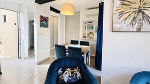 A modern living room with a blue armchair, a dining area with a wooden table and chairs, and a large artwork on the wall. - Ground Floor Apartment, 3 Rooms, 2 Terraces, 100m from Beach, A/C, Parking, WiFi Optional (Lumio)