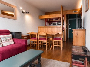 A cozy living area with a wooden dining table, chairs, a red sofa, and a bench.