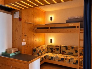 A wooden cabin interior with a bunk bed, a sofa, a desk, and a calendar on the wall.
