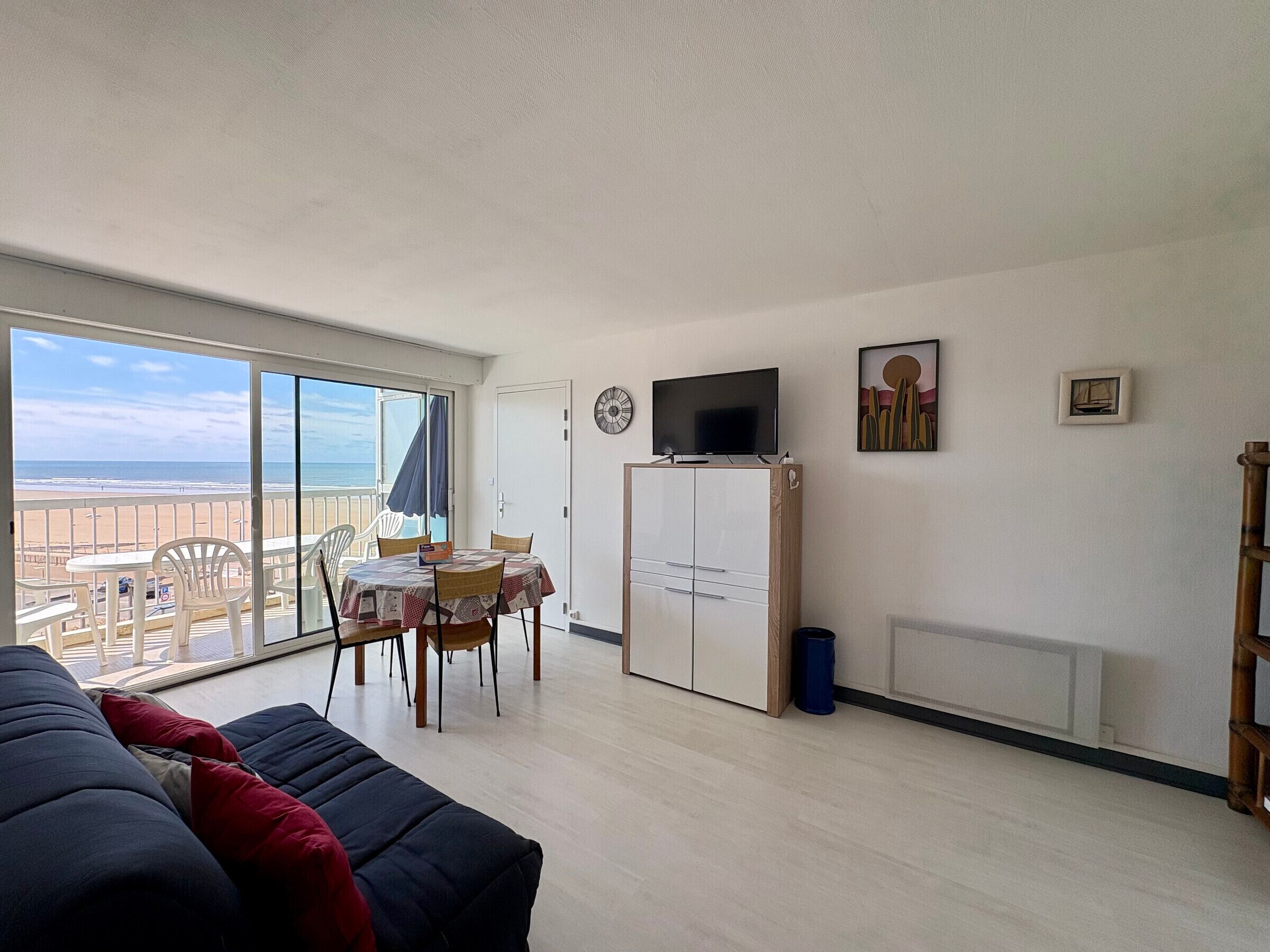 Una habitación con balcón, mesa de comedor, sillas, sofá, televisor y armario.
