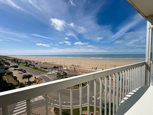 A balcony with a view of a beach, a road with cars, and a clear sky.