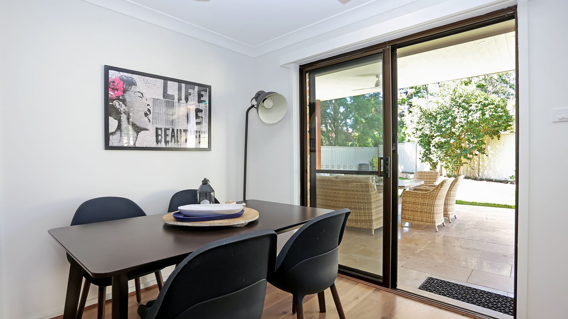A dining area with a table and chairs, a framed artwork on the wall, and a sliding glass door leading to an outdoor patio.