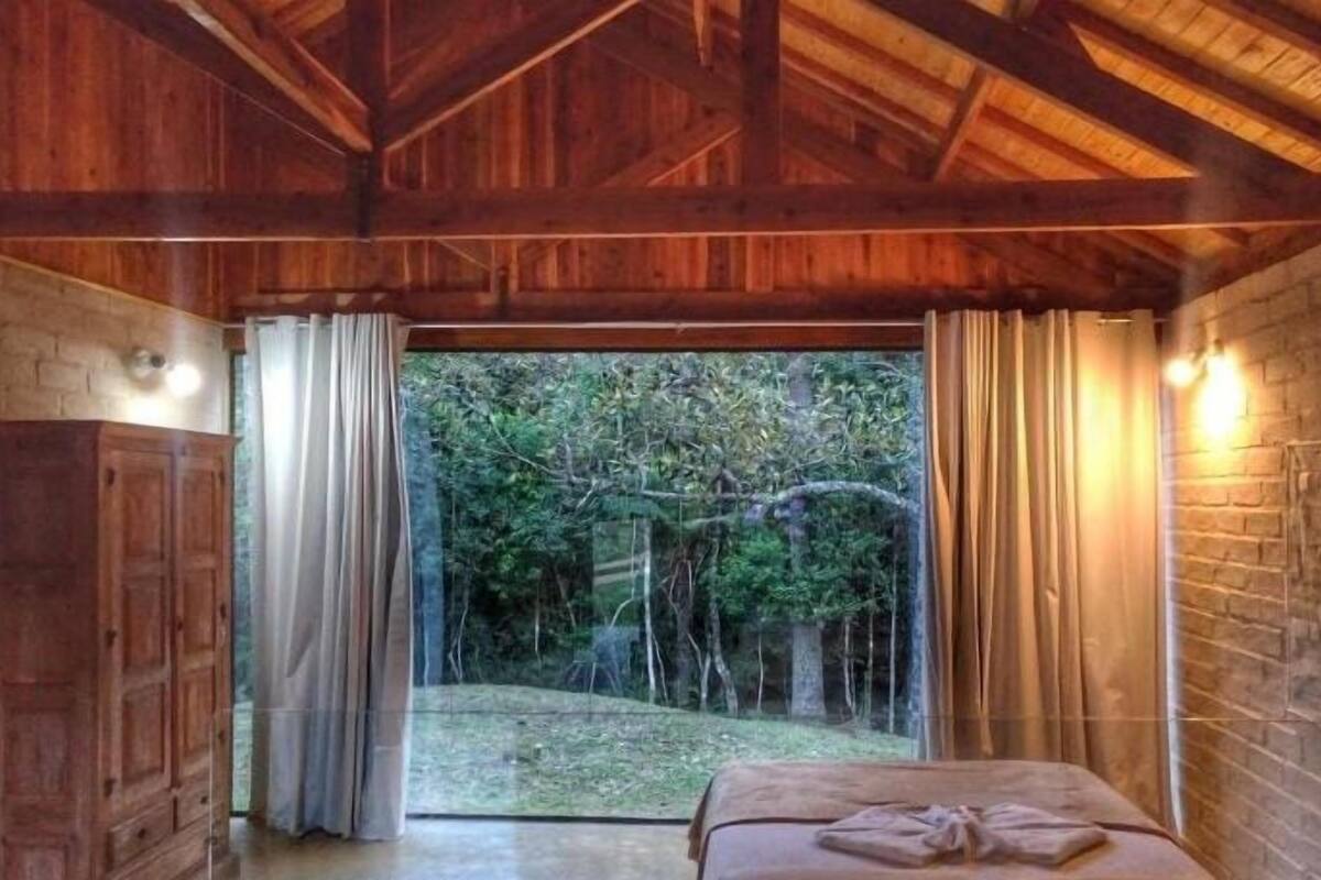 A wooden room with a bed, curtains, and a view of trees.