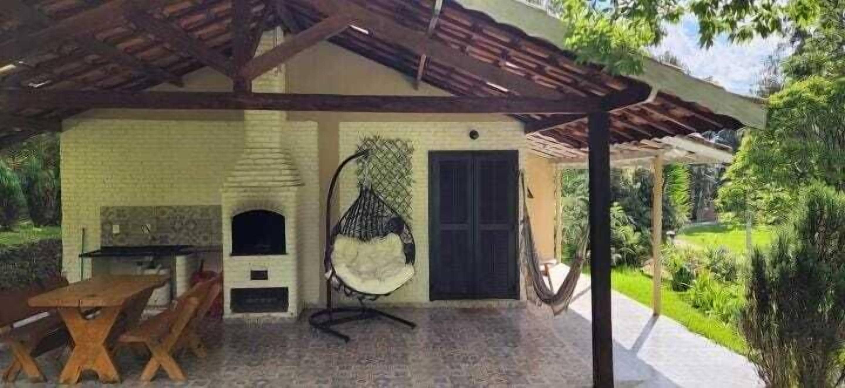 A covered patio with a brick wall, a hanging chair, a table, and a door.