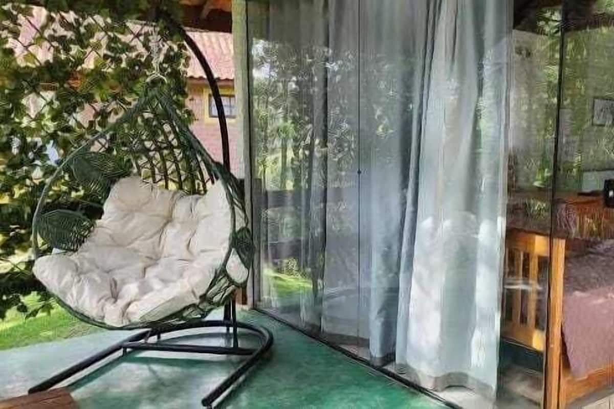 A room with a bed, a hanging chair, and a view of greenery outside.