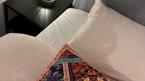 A neatly made bed with a patterned pillow, a bedside lamp on a small table, and a grey headboard. - Chalet Quattro in Bosrijke Omgeving Anloo (Anloo)