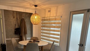 A modern living room with a round dining table, grey chairs, a hanging light fixture, and a sliding glass door. - Chalet Quattro in Bosrijke Omgeving Anloo (Anloo)