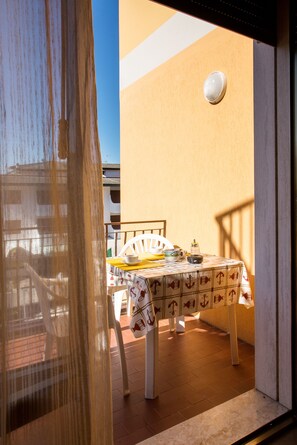 A sunlit outdoor dining area with a table set for two, a white chair, and a small table lamp.