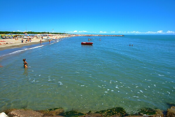 A beach with clear water, a red boat, and umbrellas.