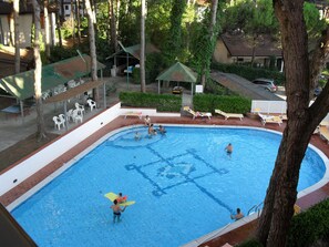 A swimming pool with people, lounge chairs, and a covered seating area.