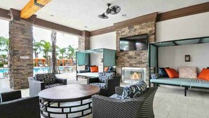 An outdoor lounge area with wicker furniture, a round table, a flat-screen TV, and a fireplace. - 7495 OL - Solterra Resort (Davenport)