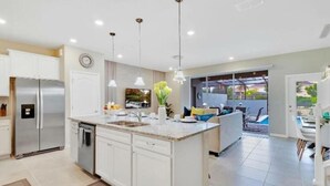 A modern kitchen with a central island, stainless steel appliances, pendant lighting, and a view to a patio area. - 7495 OL - Solterra Resort (Davenport)