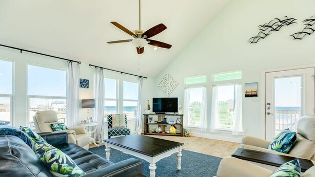 A spacious living room with a ceiling fan, a television, and a view of the ocean. - Saltwater Soul - Cool Unique Mid-Level Hangout Area! (Surfside Beach)