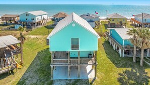 A coastal property with a prominent turquoise house featuring a balcony, surrounded by other similar houses with a view of the ocean. - Saltwater Soul - Cool Unique Mid-Level Hangout Area! (Surfside Beach)