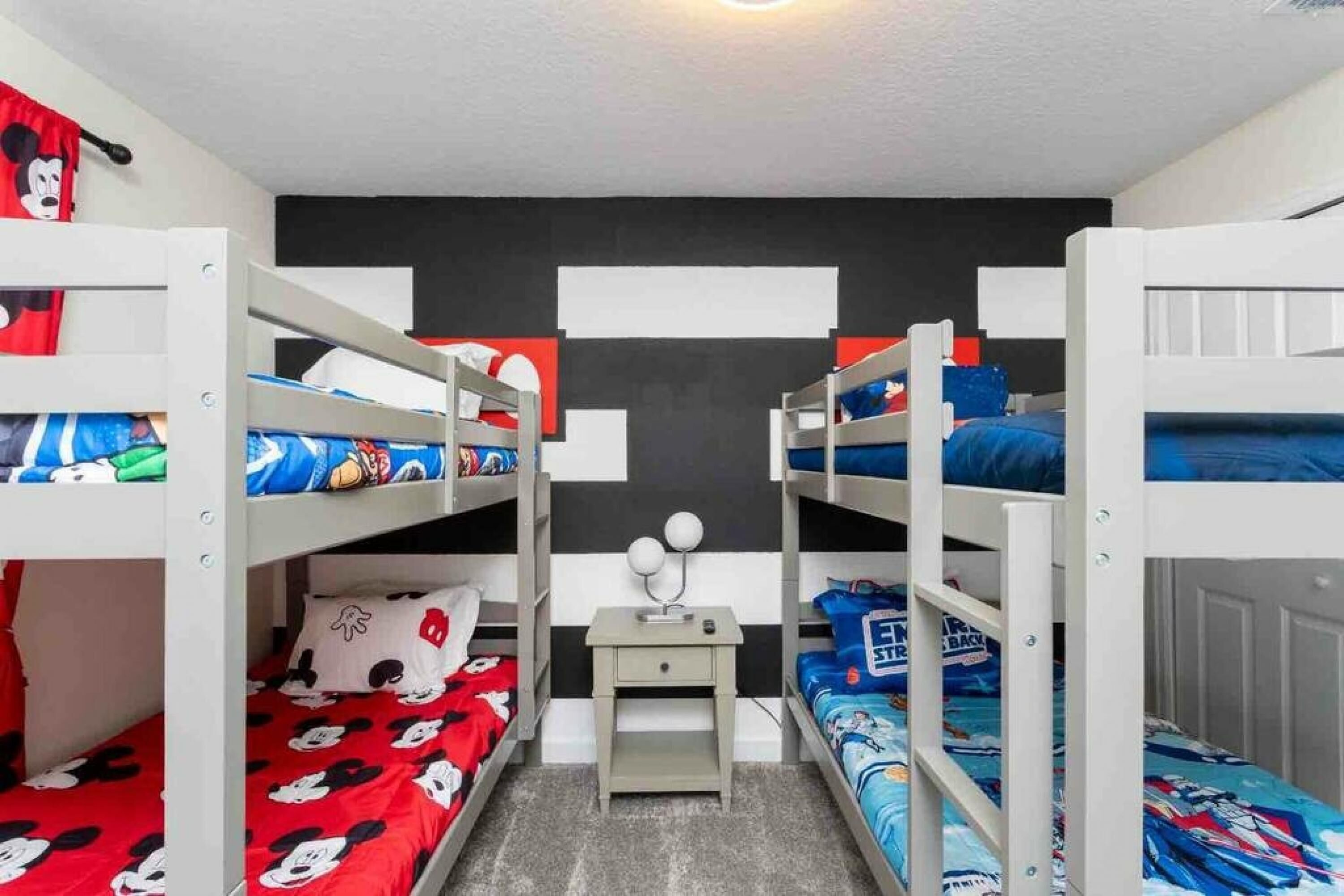 Een slaapkamer met stapelbedden, beddengoed met Mickey Mouse thema, een klein bureau met lamp en een zwart-wit gestreepte muur.