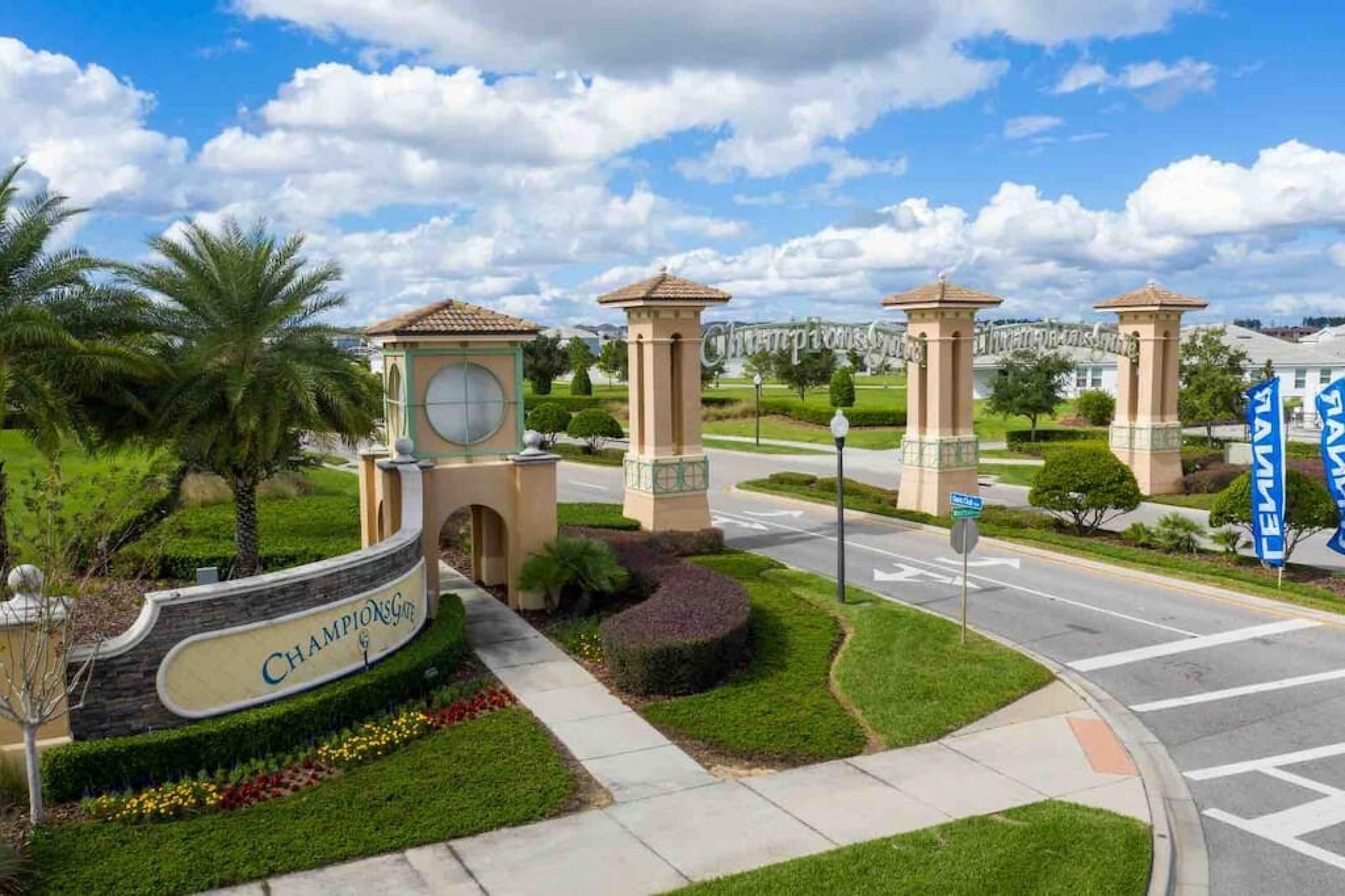 A landscaped entrance with a sign reading "ChampionsGate," palm trees, and a road with a blue sign.