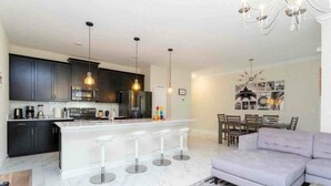 A modern kitchen with dark cabinets, a white island with bar stools, and pendant lighting. - 1144 CD - Champions Gate (Davenport)