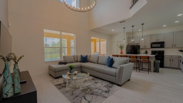 A spacious living room with a sectional sofa, a glass coffee table, and a modern chandelier. - 1078 OC - Watersong in Davenport (Davenport)