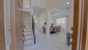 A spacious interior with a staircase leading to a second floor, a dining area with wooden chairs and a table, and a kitchen in the background. - 1078 OC - Watersong in Davenport (Davenport)