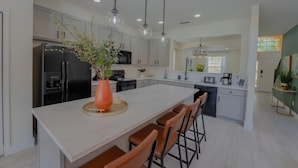 A modern kitchen with white cabinets, a large island with bar stools, a black refrigerator, and pendant lighting. - 1078 OC - Watersong in Davenport (Davenport)