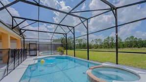 A swimming pool with a hot tub, surrounded by a covered area with a metal frame and glass walls, set against a grassy landscape. - 1078 OC - Watersong in Davenport (Davenport)