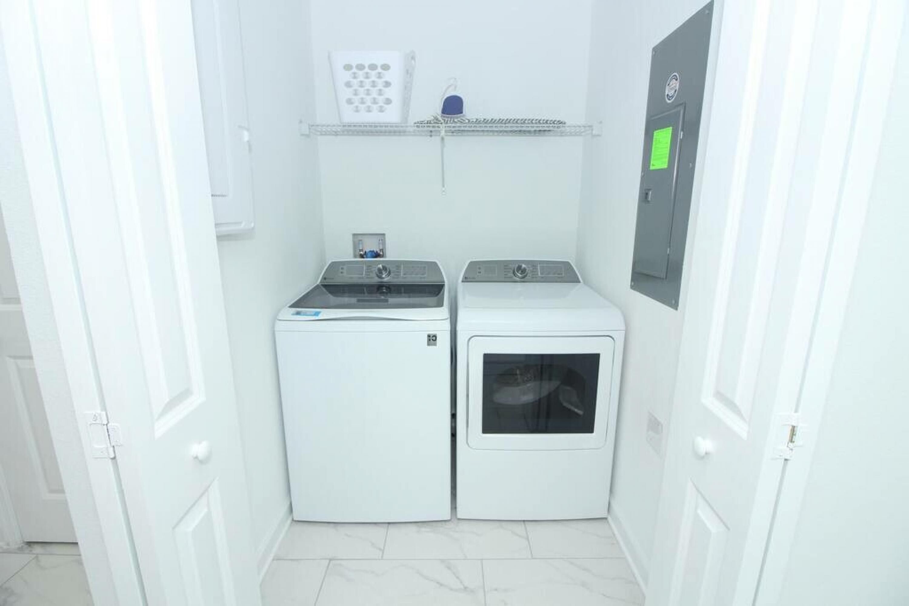 A compact laundry room with two washing machines and a dryer, a small shelf with a control panel, and a door with a lock.