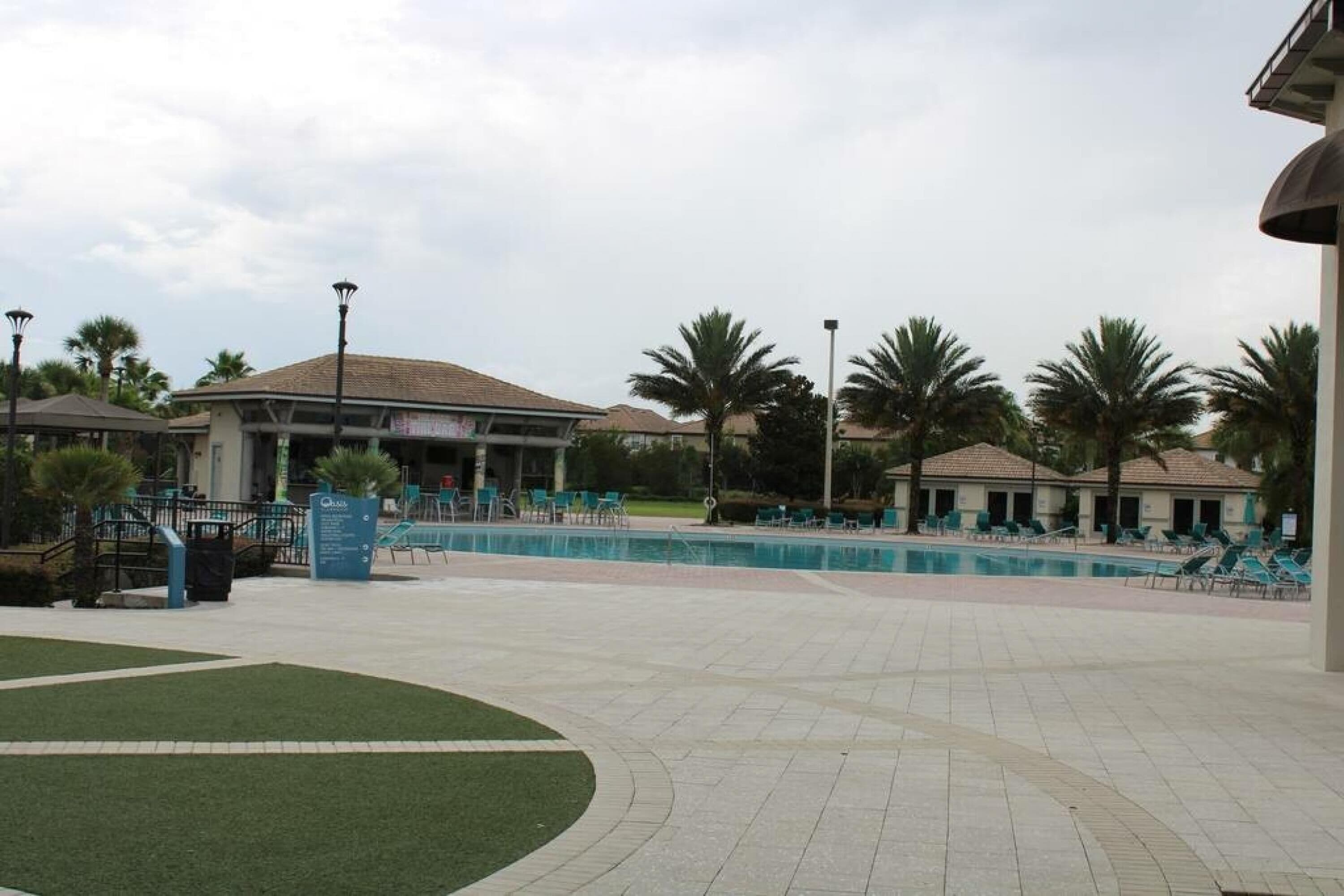 Zona de piscina con sillones de descanso y palmeras.