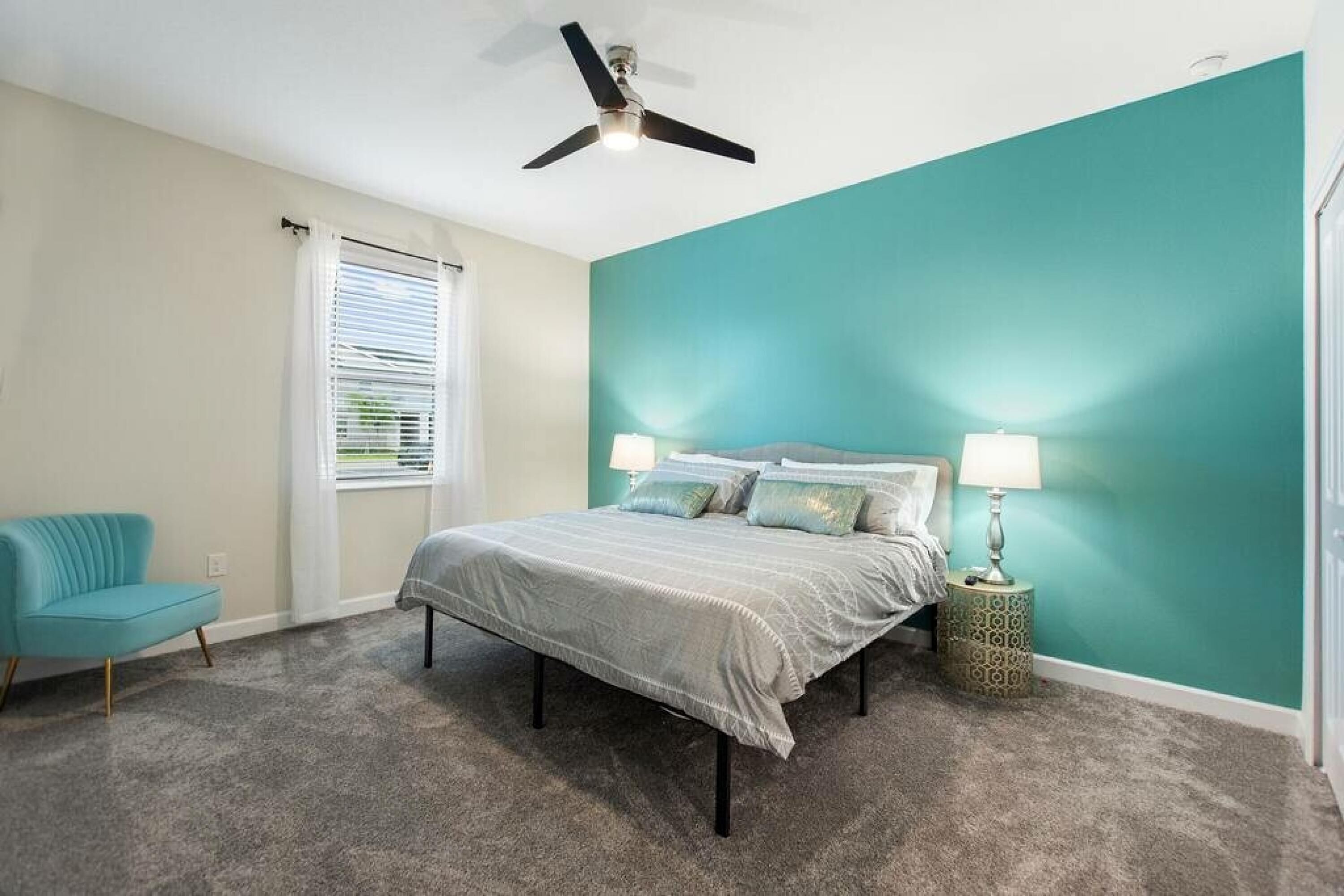 A bedroom with a bed, a chair, a ceiling fan, and a window with blinds.
