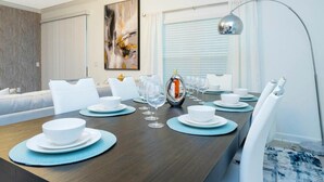 Un coin repas avec une table en bois dressée pour six personnes, des chaises blanches et un luminaire suspendu moderne.