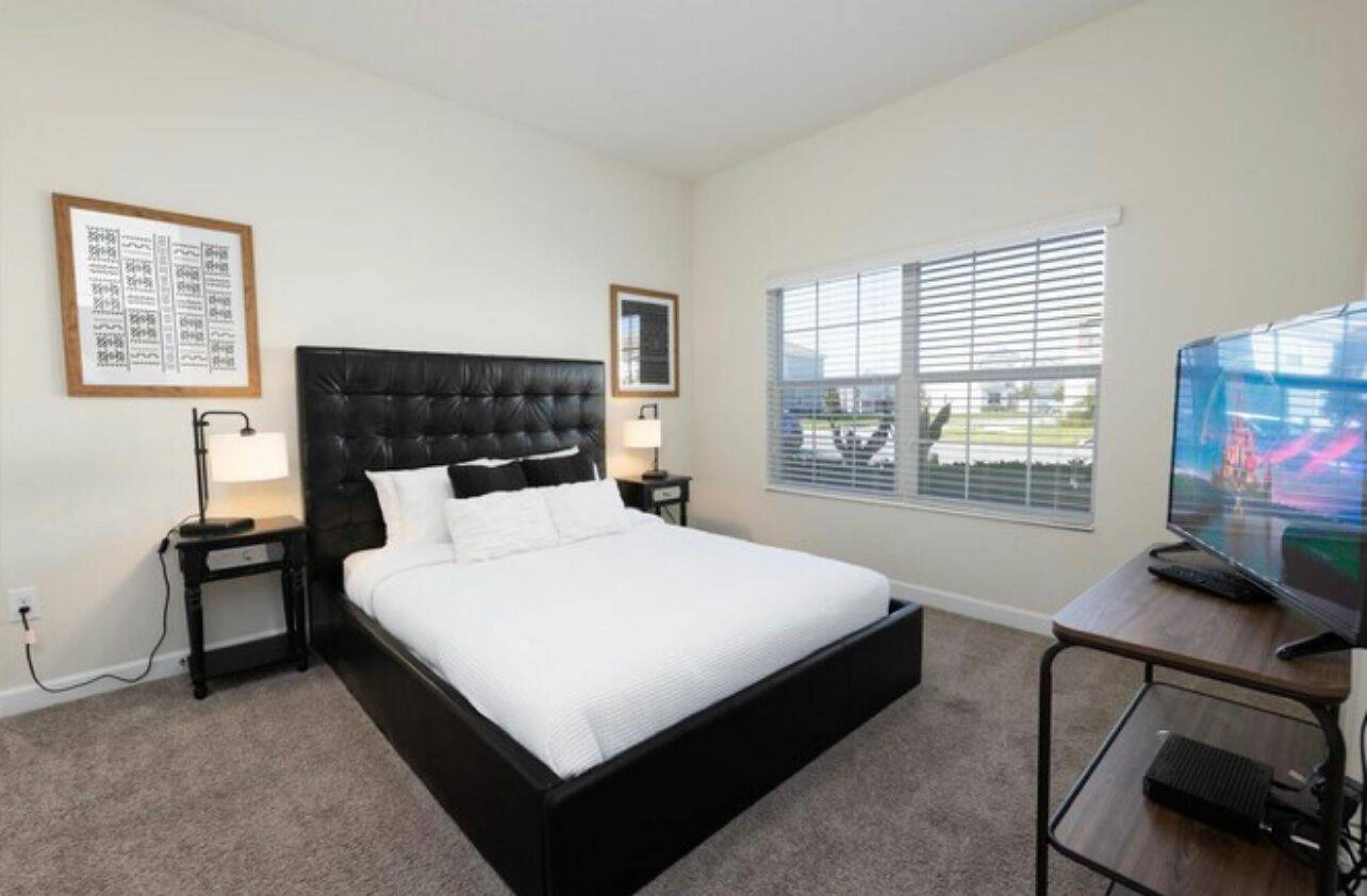 A bedroom with a large bed, a desk with a computer, a TV, and a window with blinds.