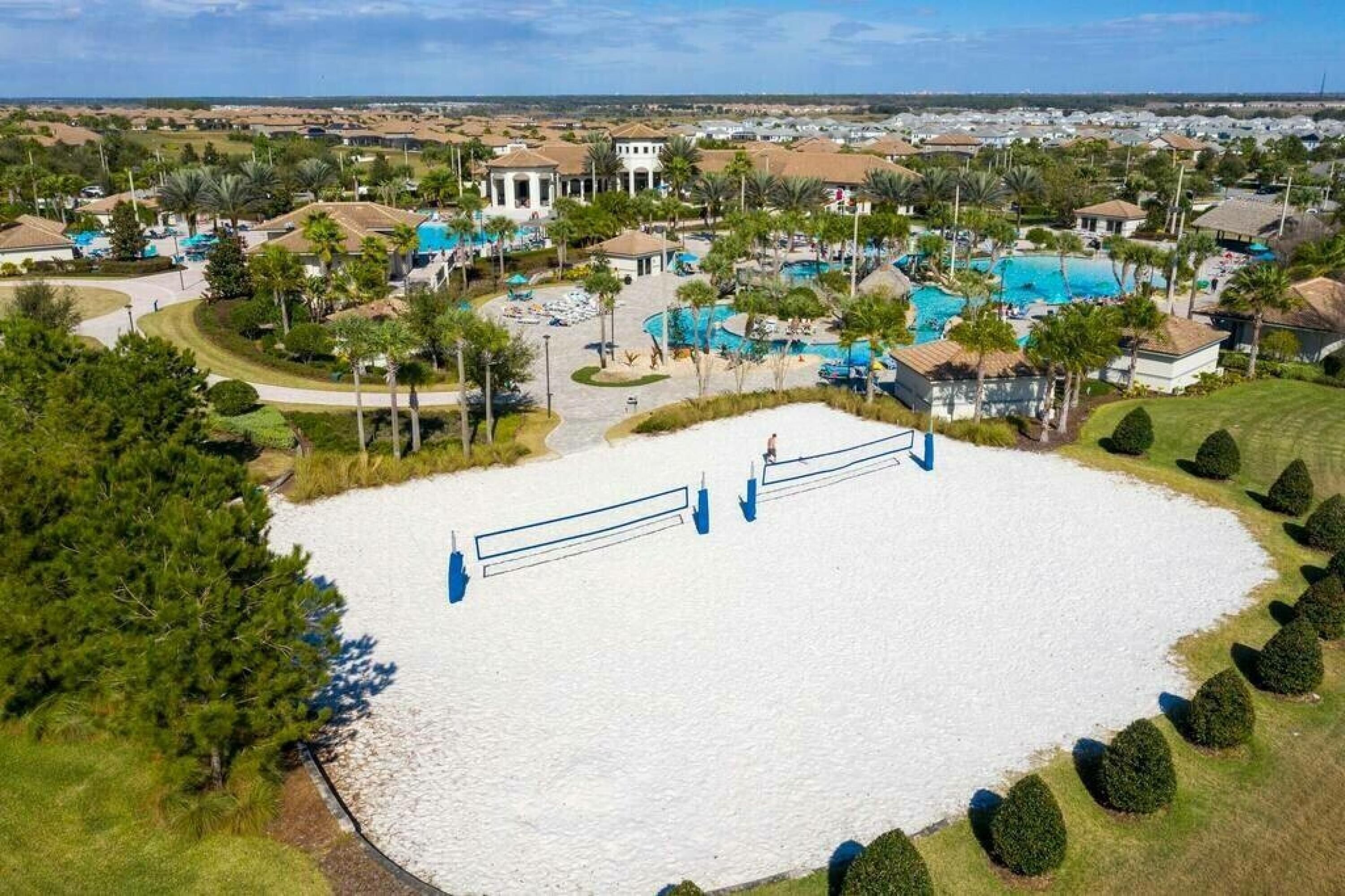 Vista aérea de un complejo turístico con múltiples piscinas, una cancha de tenis y una extensa zona de arena blanca.