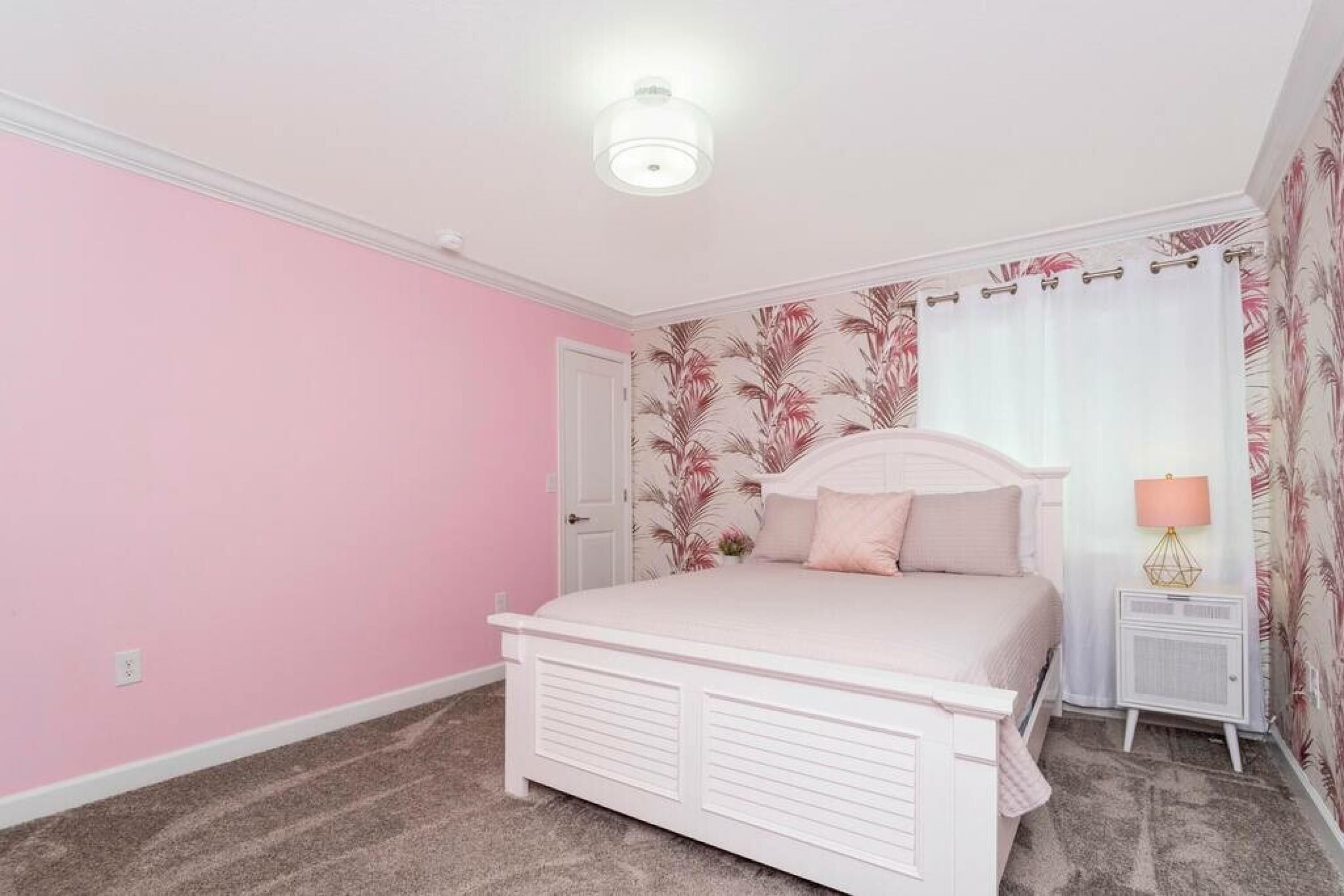 A bedroom with a white bed, pink walls, and a floral wallpaper pattern.
