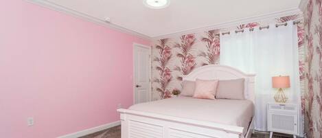 A bedroom with a white bed, pink walls, and a floral wallpaper pattern.