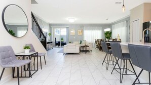 Ein modernes Wohnzimmer mit einer Couch, Sesseln, einem Essbereich und einer Treppe.