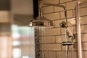 A showerhead with water running, a handheld shower attachment, and a tiled wall.