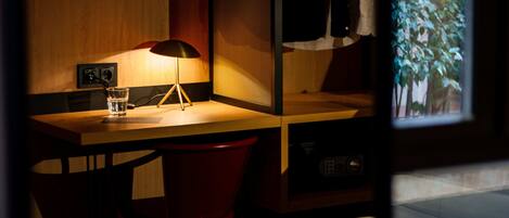 A hotel room with a wooden desk, a lamp, a glass of water, and a red bucket.