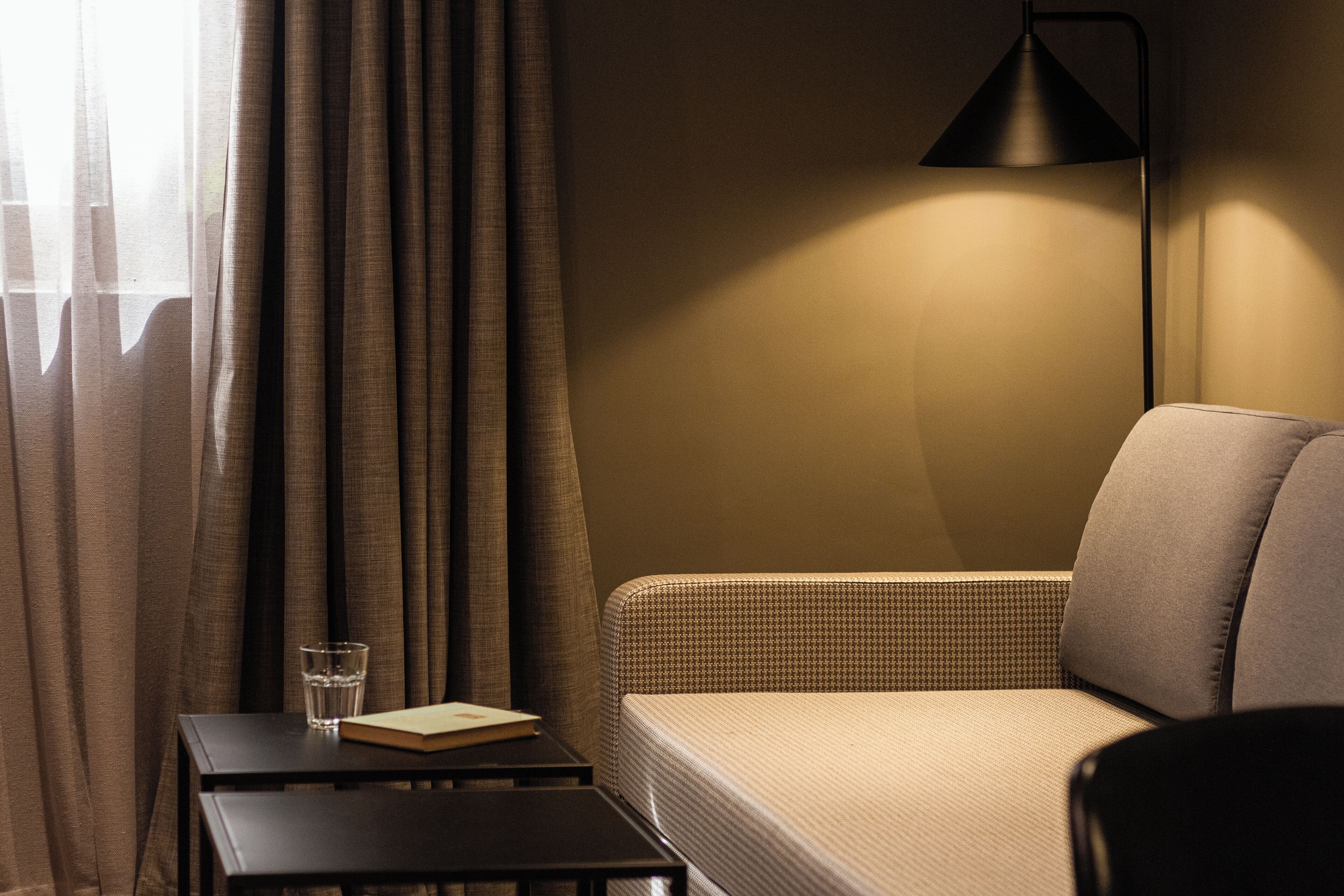 Ein Hotelzimmer mit einer Couch, einem kleinen Tisch mit einem Glas Wasser und einem Buch sowie einer Lampe.