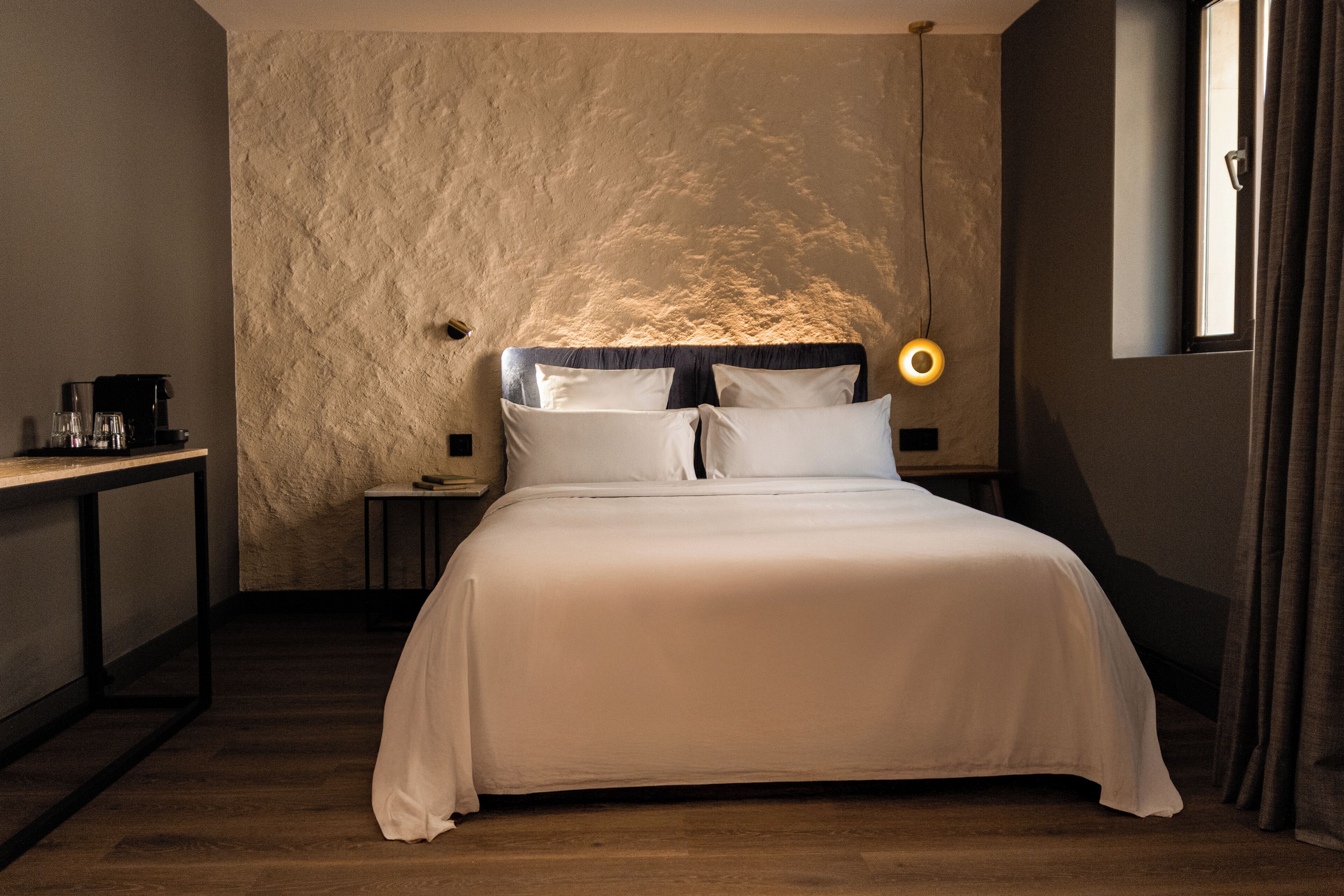 Ein Schlafzimmer mit einem großen Bett, einem Nachttisch mit Lampe und einem Fenster mit Vorhängen.