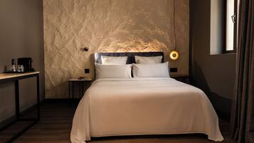 A bedroom with a large bed, a bedside table with a lamp, and a window with curtains.