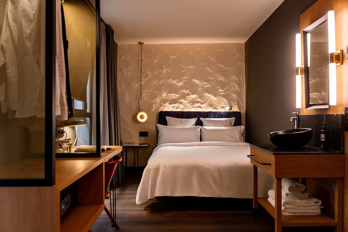 Une chambre d’hôtel comprenant un lit, une table de chevet, un miroir et une étagère avec des serviettes.